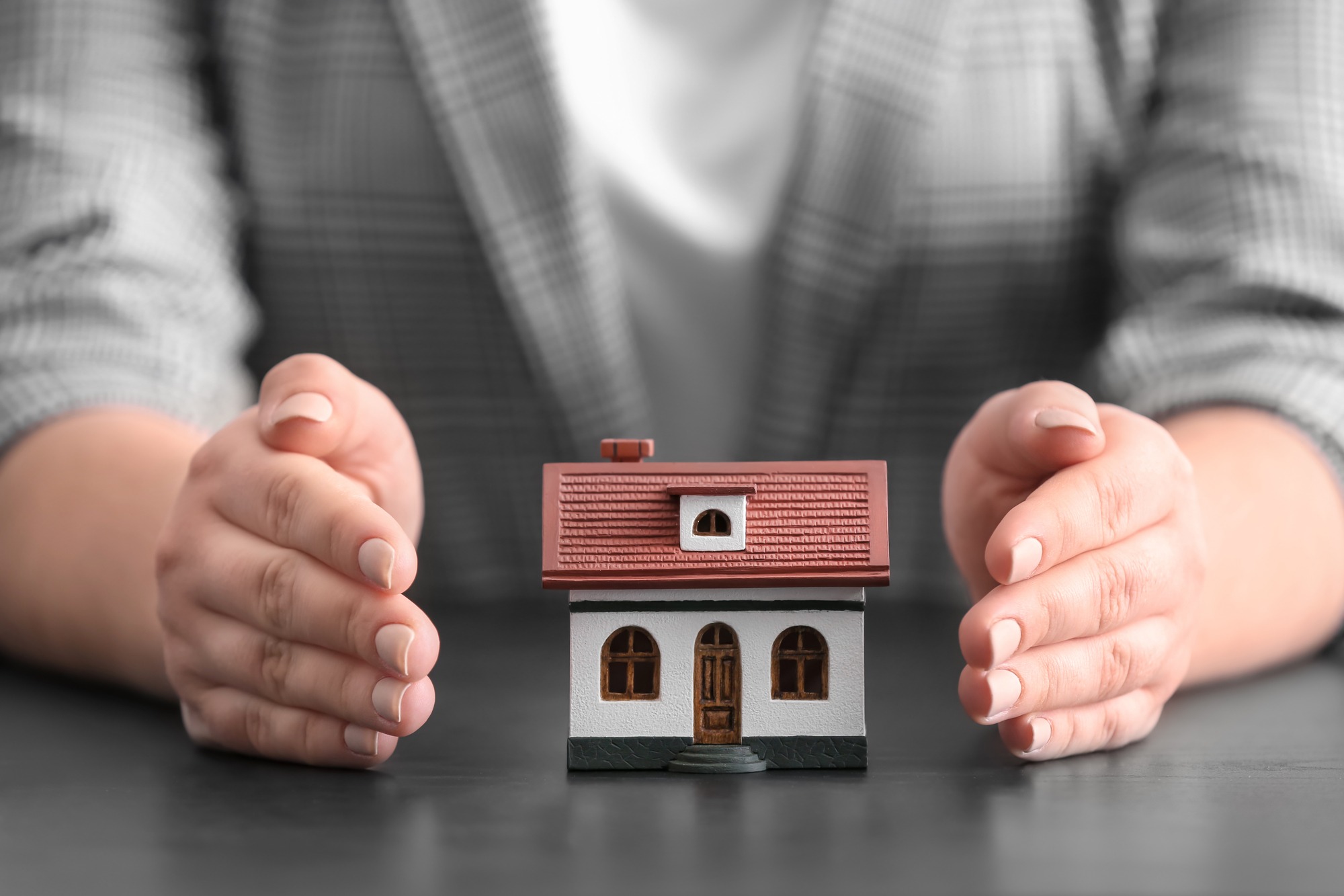 Insurance Concept. Woman With Toy House at Table.